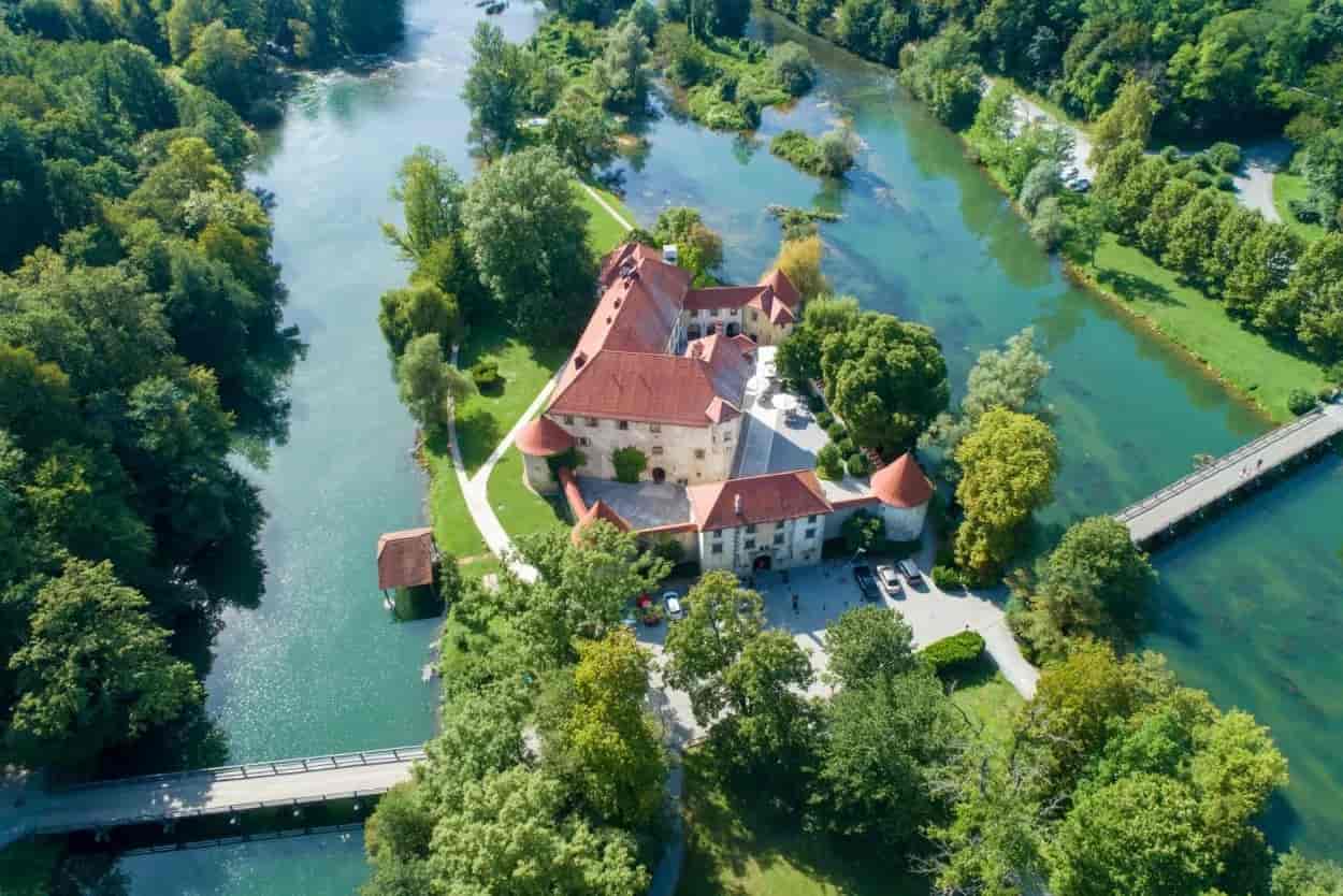 Otočec Castle on island surrounded by green trees and turquoise river, view from above