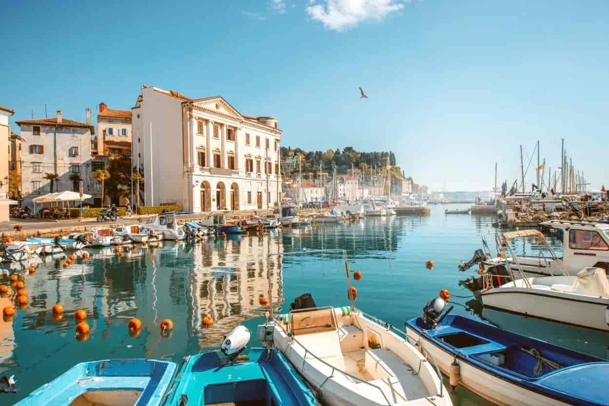 Boats moored in Piran marina with historic buildings reflecting in calm blue water