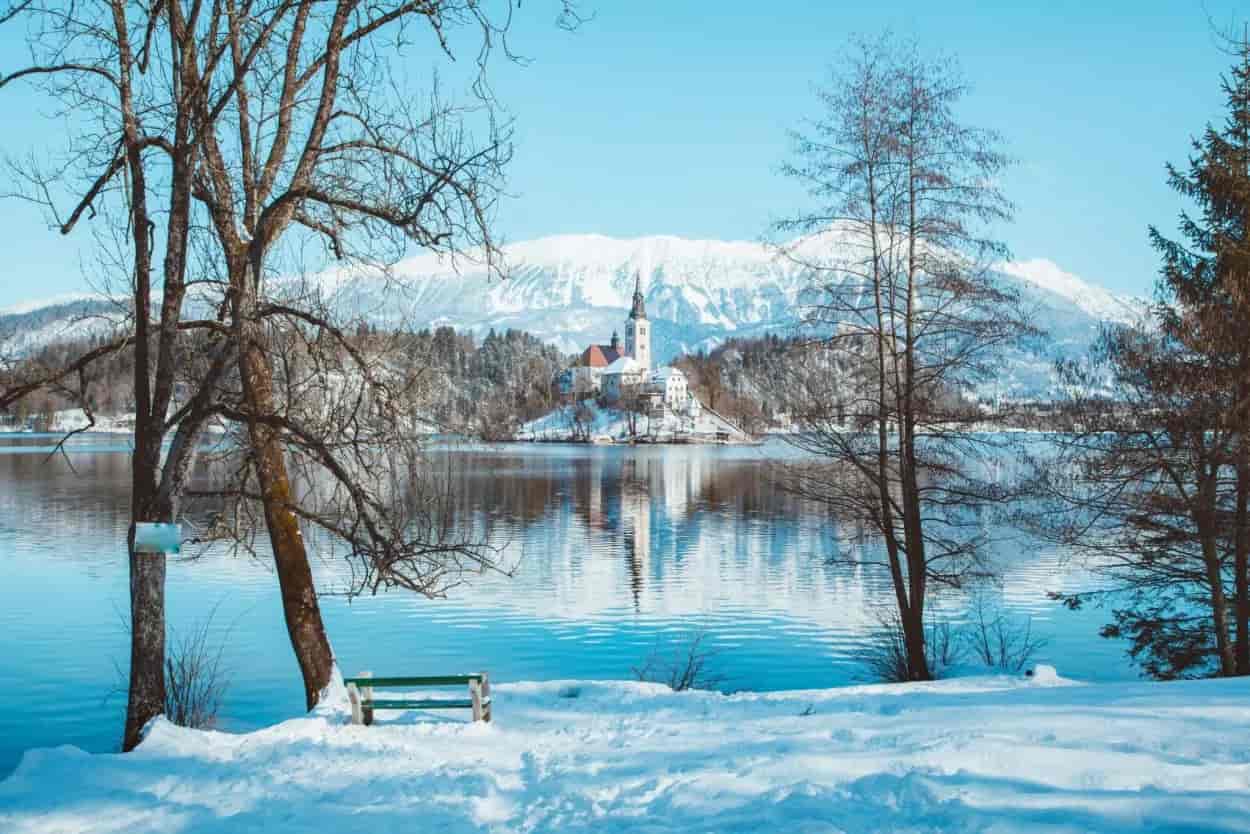 Lake Bled island church in winter with snow-capped mountains and blue water reflection