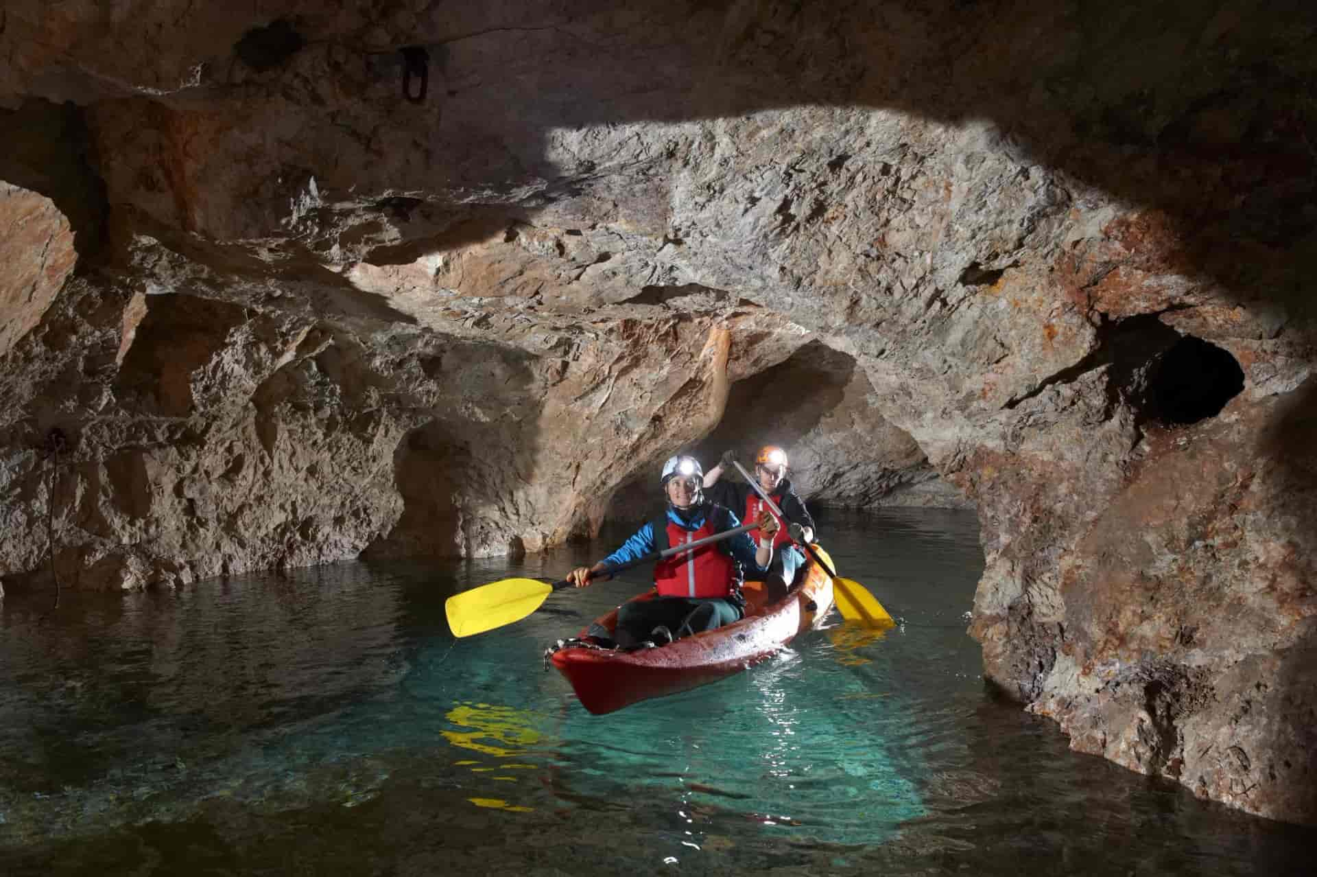 Kayaking through a dark cave with clear turquoise water and rocky walls, Mezica Mine.