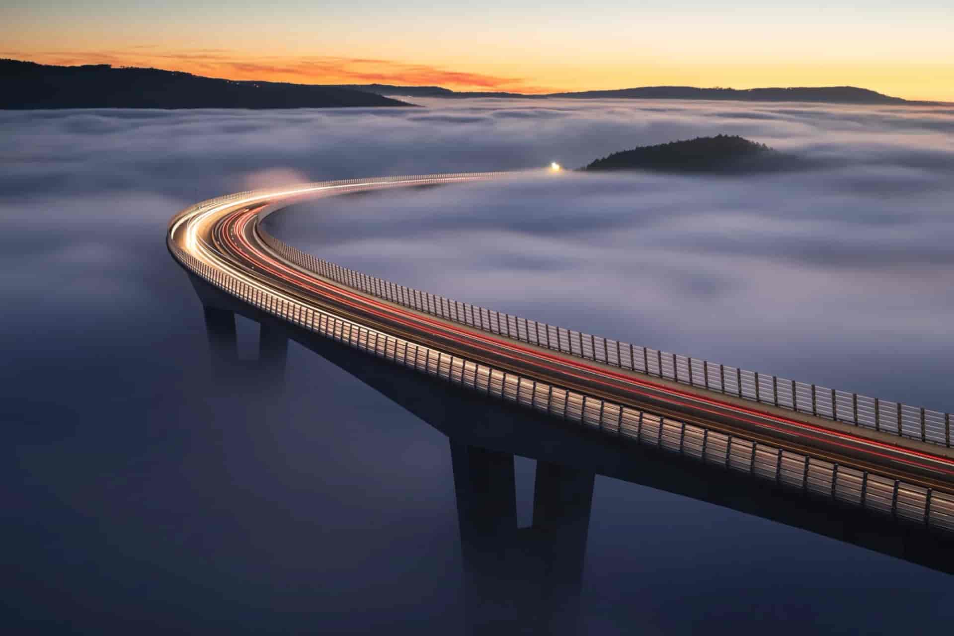Highway viaduct above thick fog at sunrise with vehicle light trails near Crni Kal.