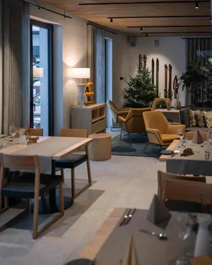 Restaurant dining area with modern wooden tables, yellow armchairs, and vintage skis by a Christmas tree.