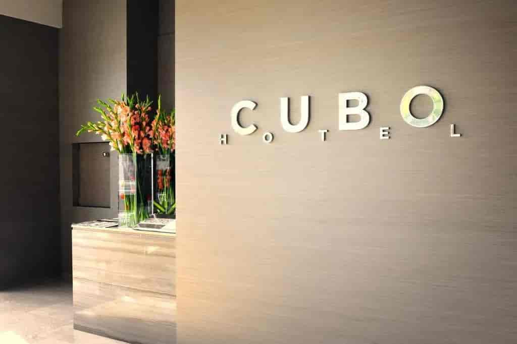 Cubo Hotel logo signage on a textured wall next to a reception desk with flowers.
