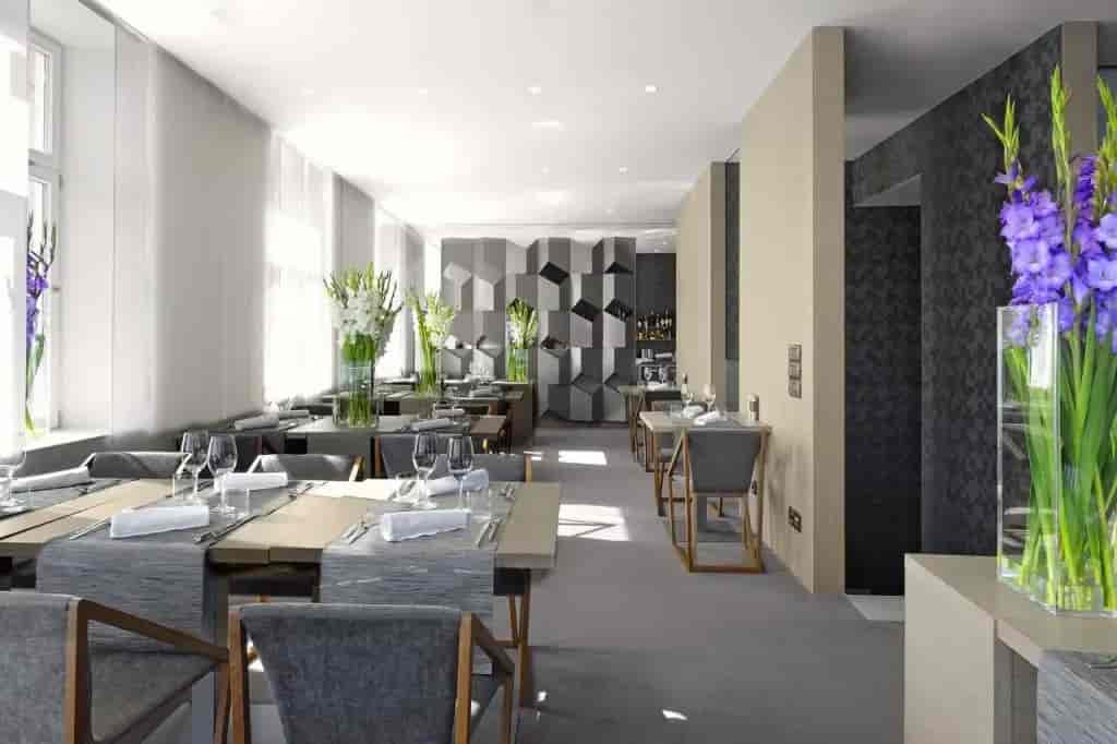 Modern hotel breakfast area with gray seating, white flowers, and geometric wall decor