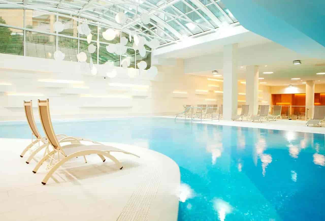Indoor swimming pool with glass roof, lounge chairs, and modern white decor in Portoroz.