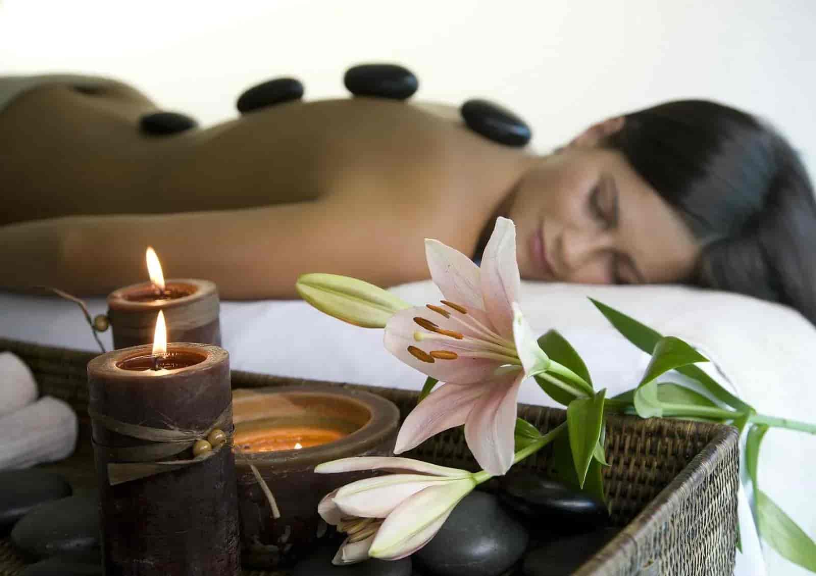Woman receiving hot stone massage with lit candles and pink lily in foreground at Wellness Park Lasko.