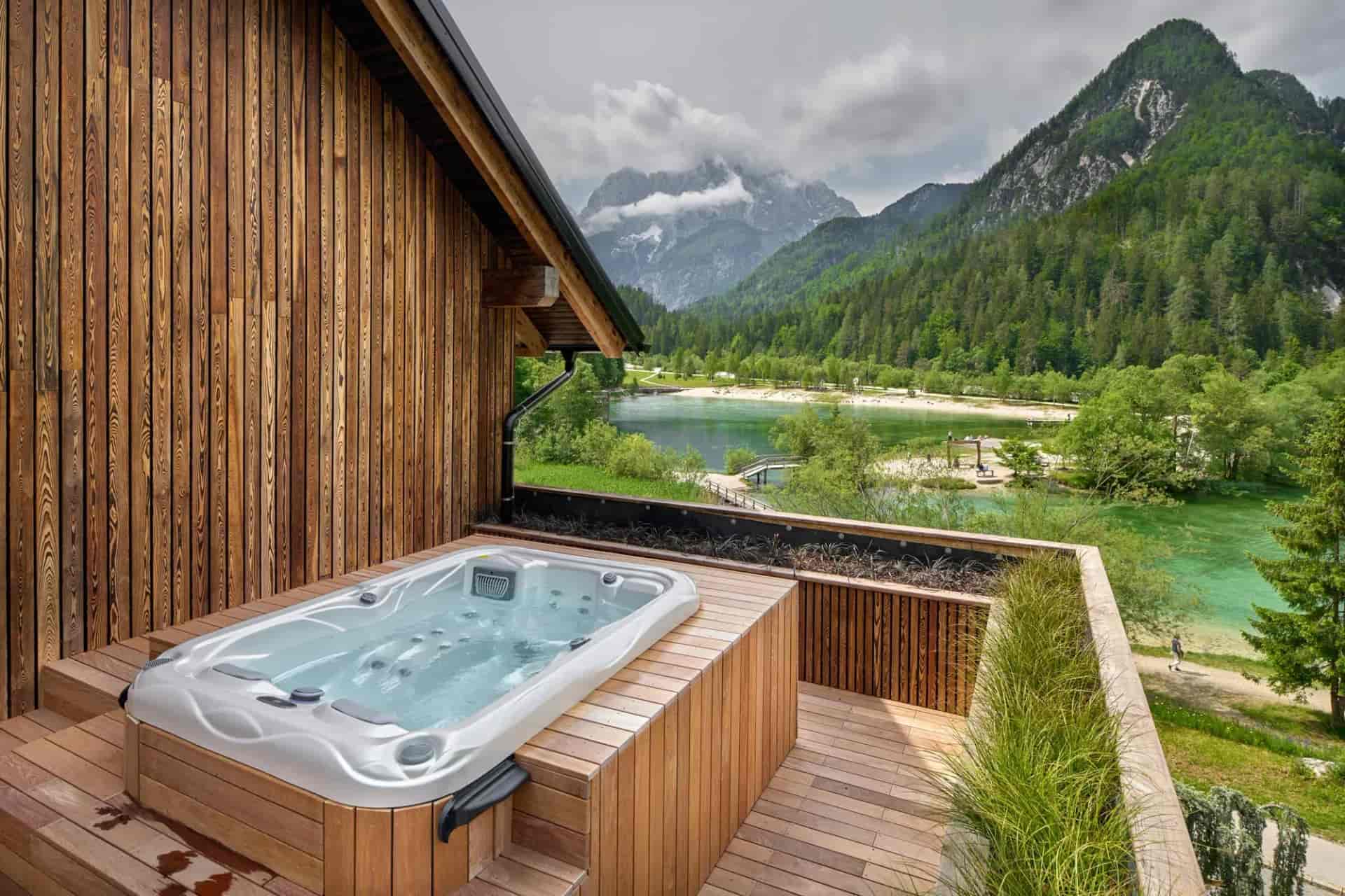 Jacuzzi on wooden deck overlooking turquoise lake and forested mountains