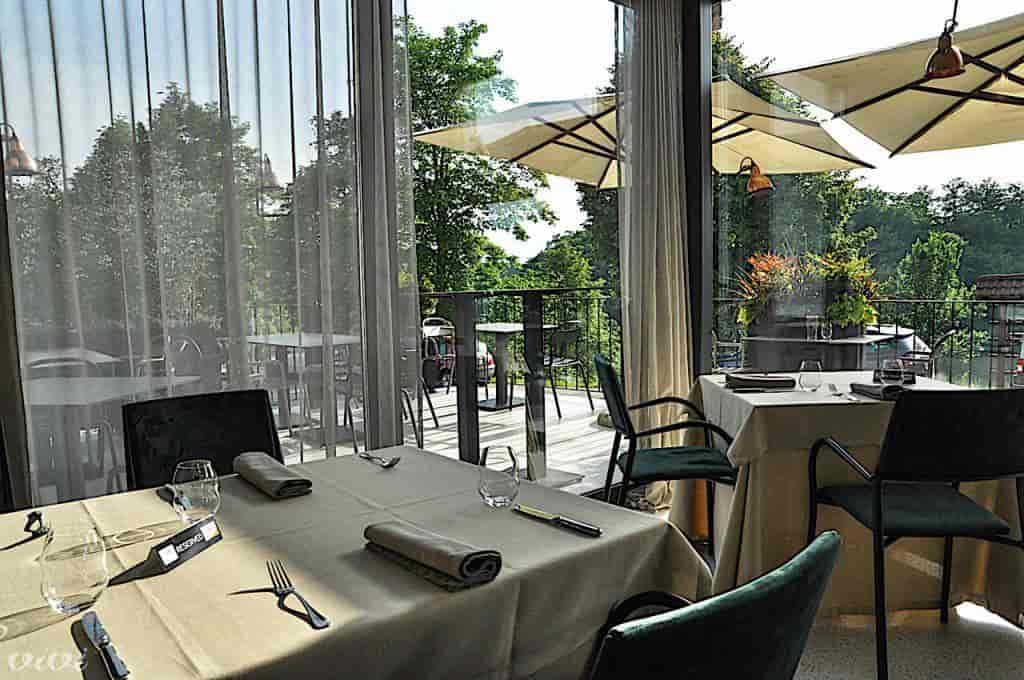 Dining area with set tables looking out onto a balcony with greenery and umbrellas