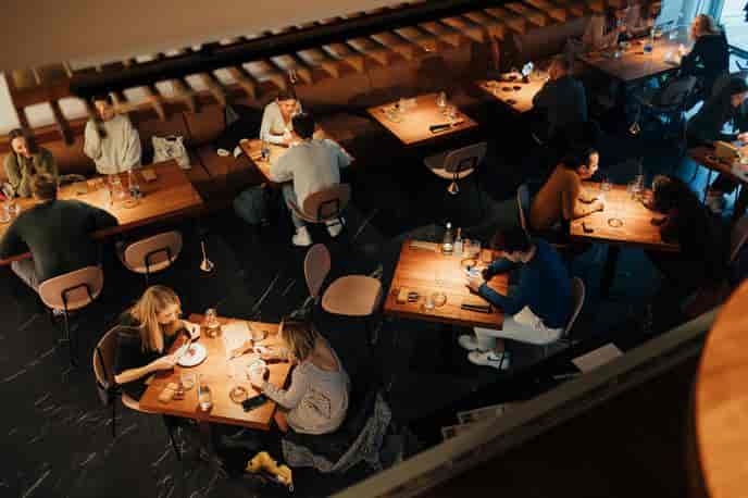 Diners seated at wooden tables inside a dimly lit, modern bistro or restaurant.
