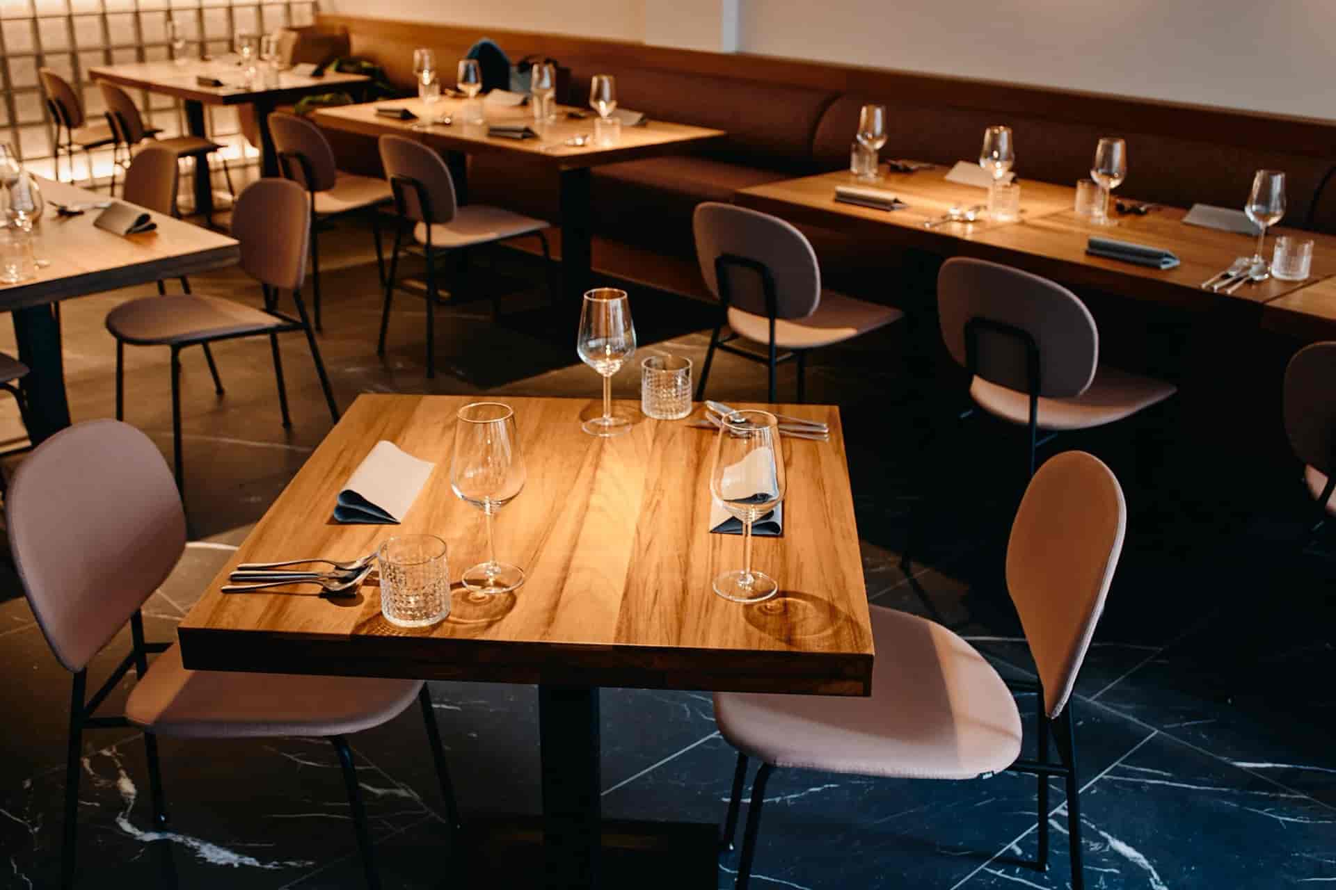 Dining tables set with wine glasses and cutlery inside a modern bistro with dark marble floors.