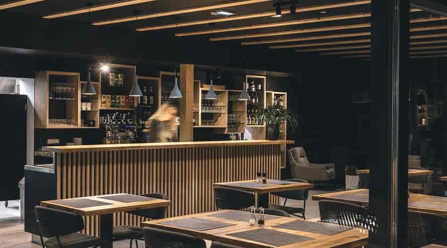Modern restaurant interior with wooden bar, dark walls, and set dining tables at Restaurant Majerca Bohinj.