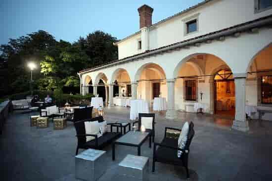 Outdoor terrace event setup with seating and arched white building at dusk