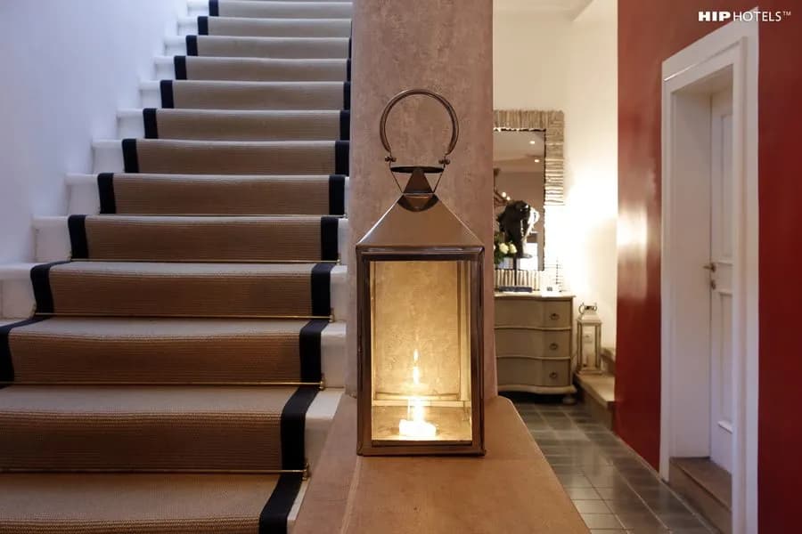 Lantern with lit candle next to carpeted staircase in hotel interior near red wall.