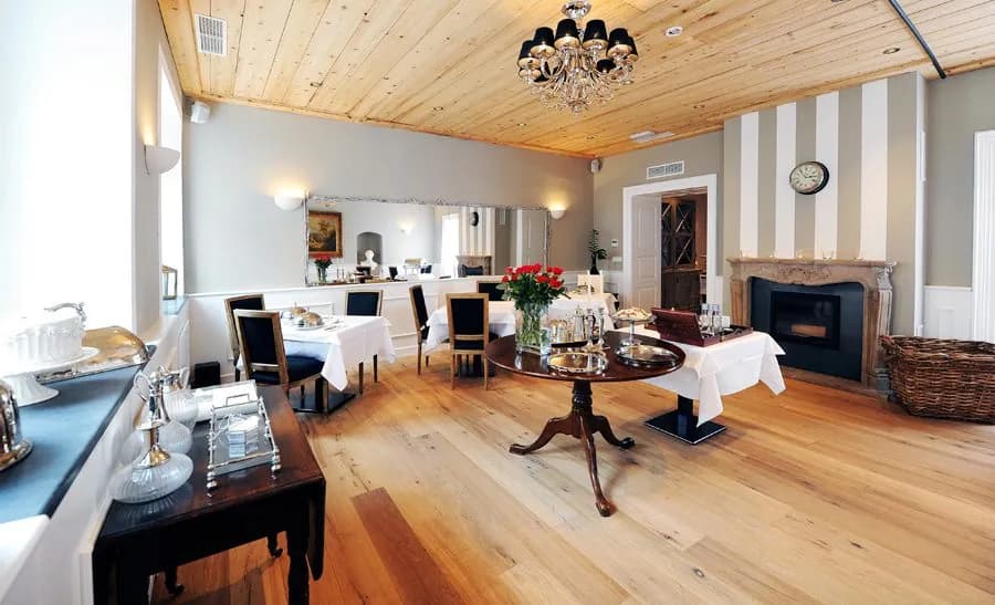 Elegant hotel breakfast room with wood floors, white linens, and a crystal chandelier.