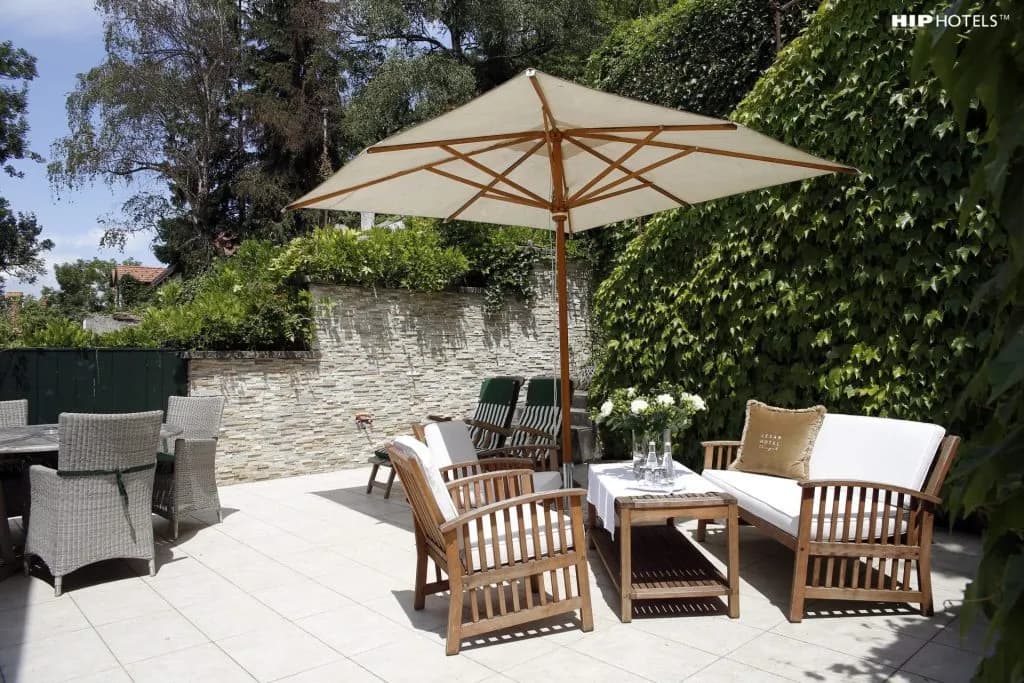 Outdoor hotel terrace with wooden seating, umbrella, and lush green ivy wall, Lesar Hotel Angel.