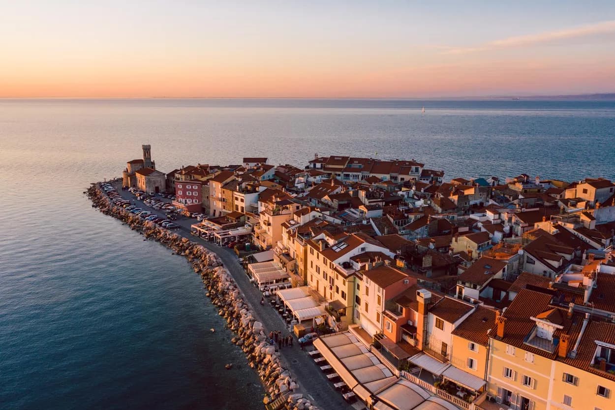 Panoramic view of Piran coastal town with red roofs and church tower at sunset over the sea.