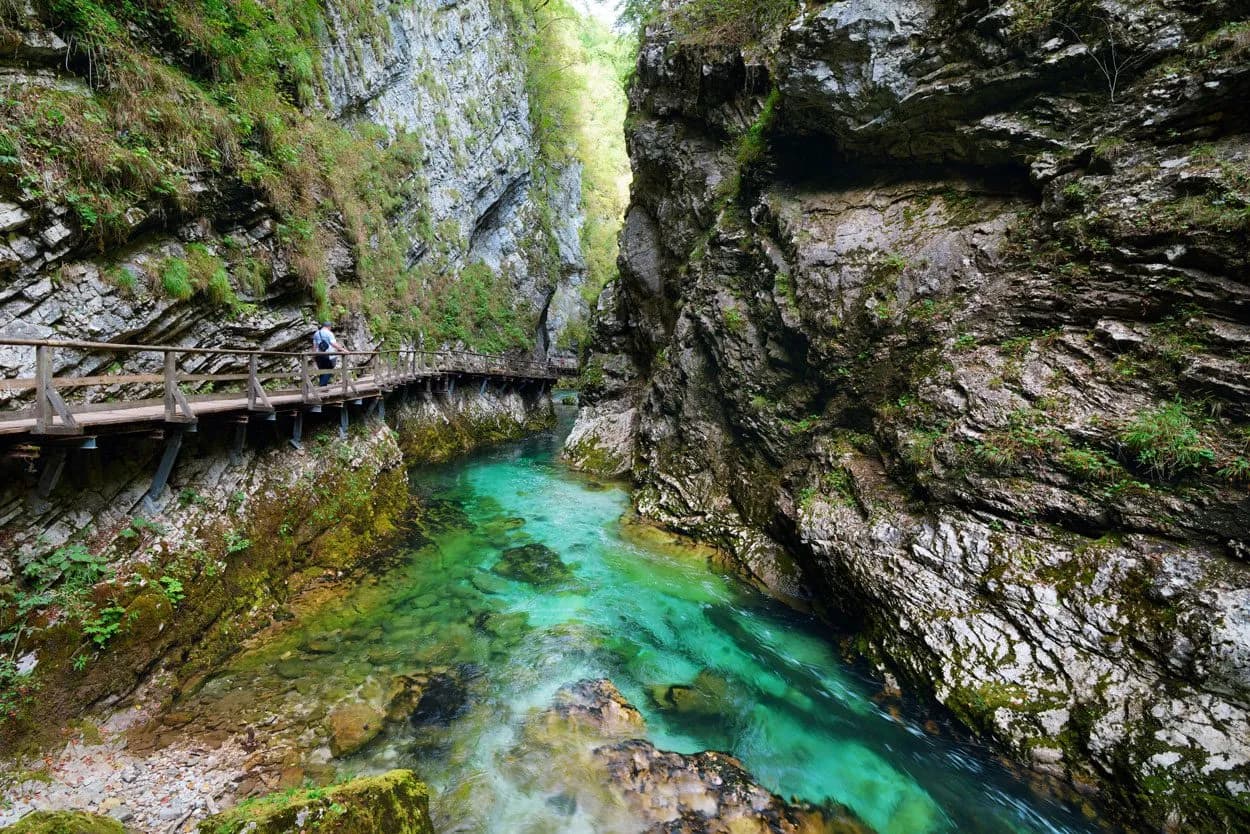 Hiking on a wooden boardwalk through Vintgar Gorge with turquoise river flowing between steep rock walls.