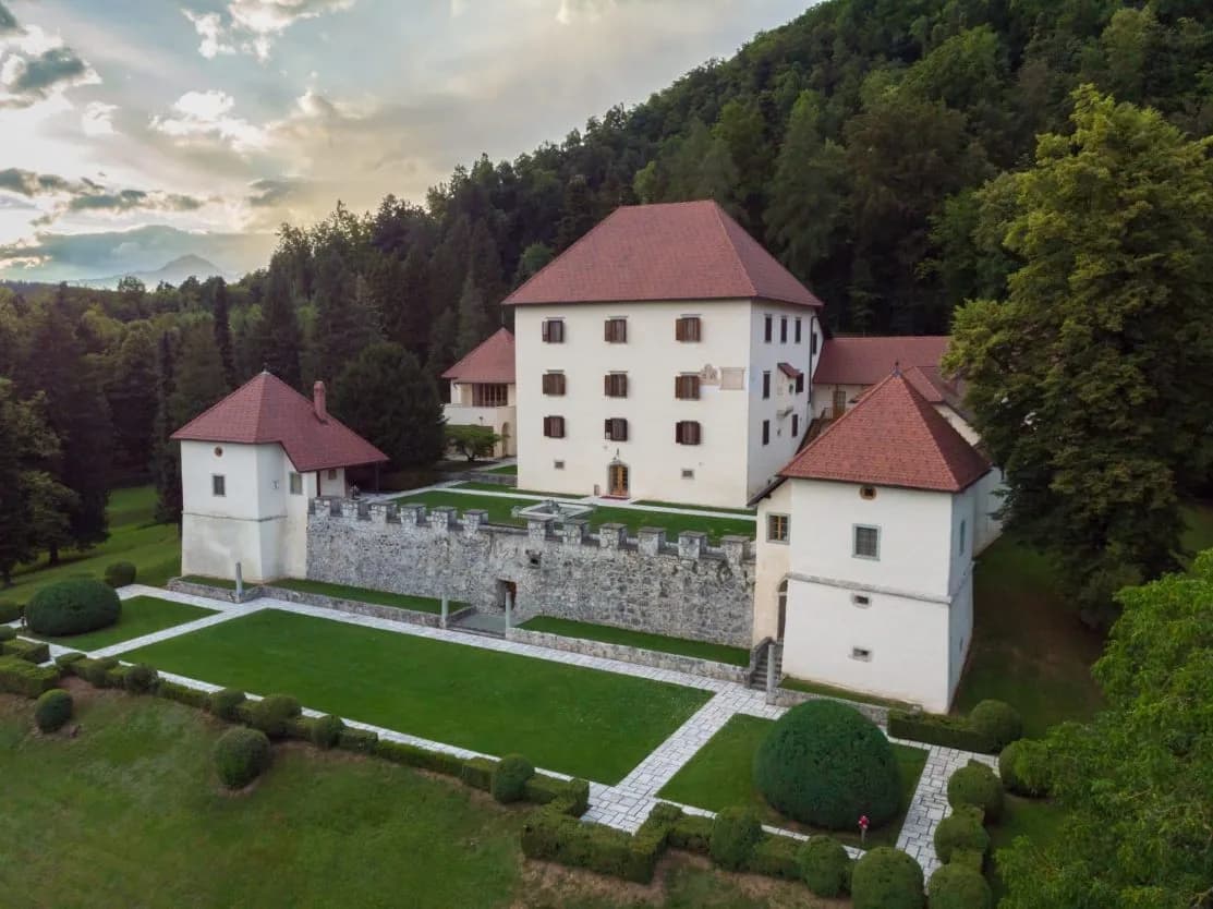 Strmol Castle with red roofs, stone walls, and manicured gardens backed by a dense forest.