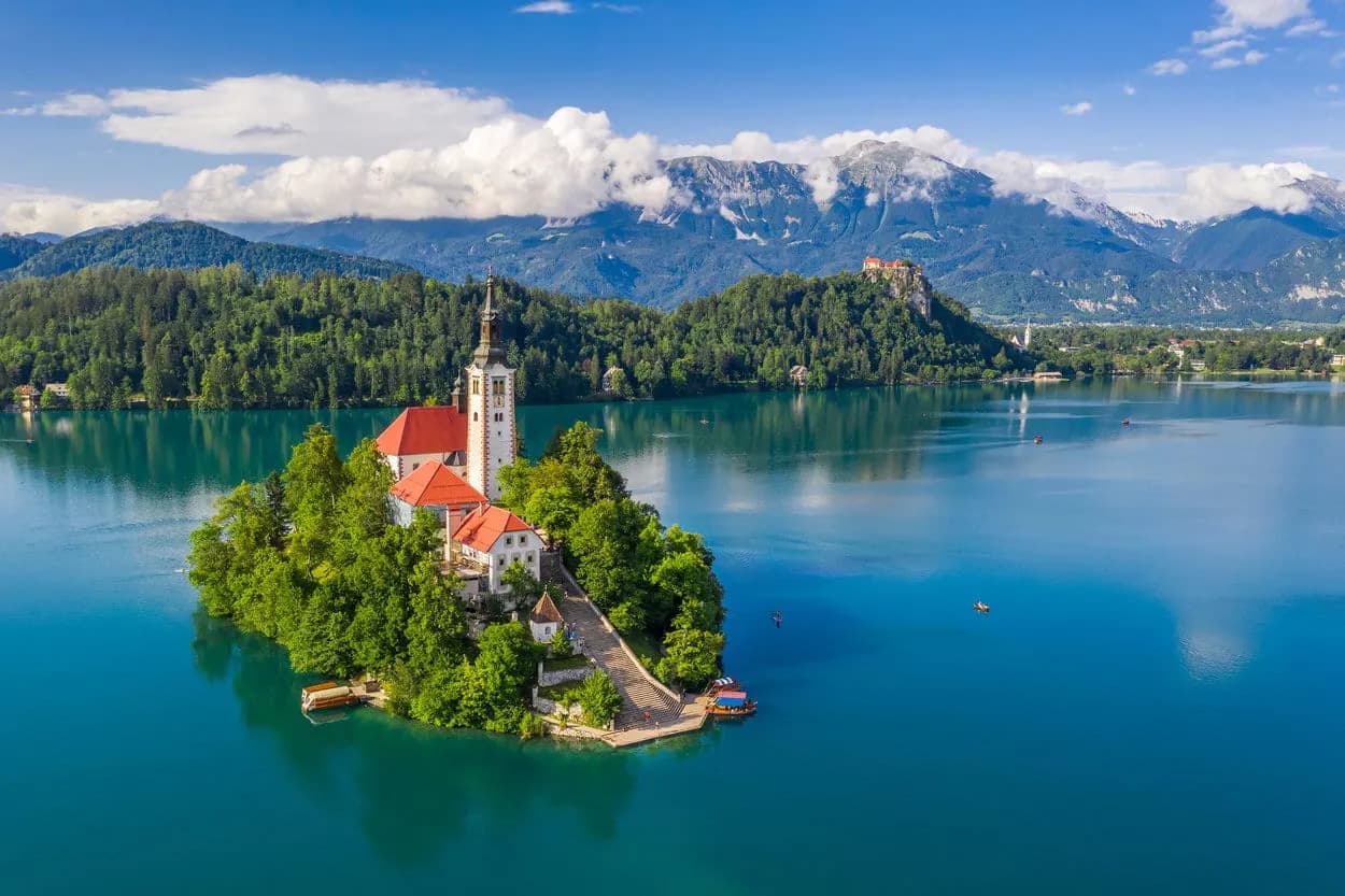 Church on Lake Bled island with turquoise water, forest, and Julian Alps mountains.
