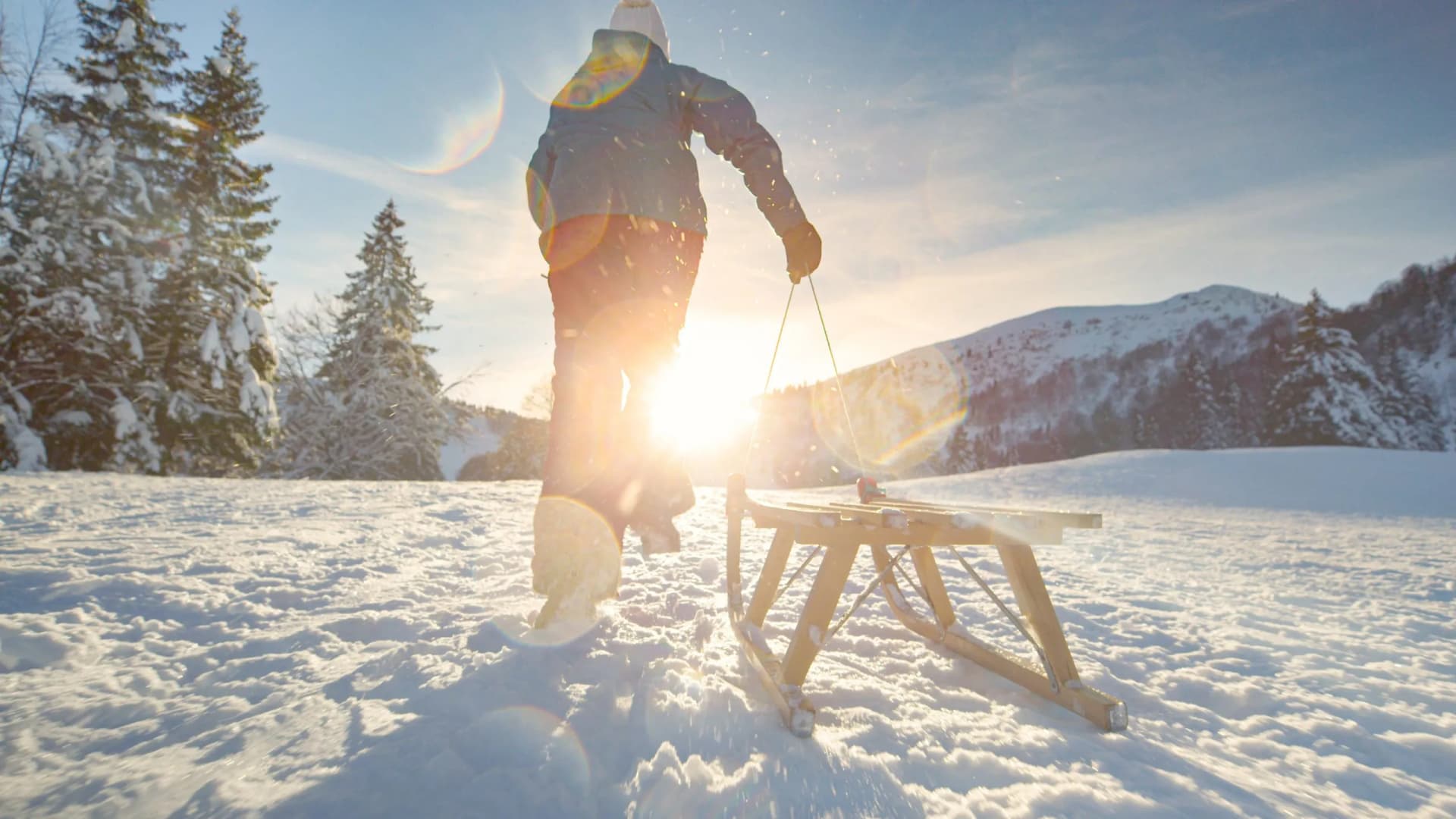Person pulling wooden sled through deep snow on sunny winter mountain slope