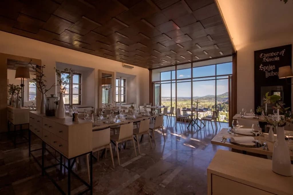 Restaurant dining room with tables set and large windows overlooking a green valley near Bled.