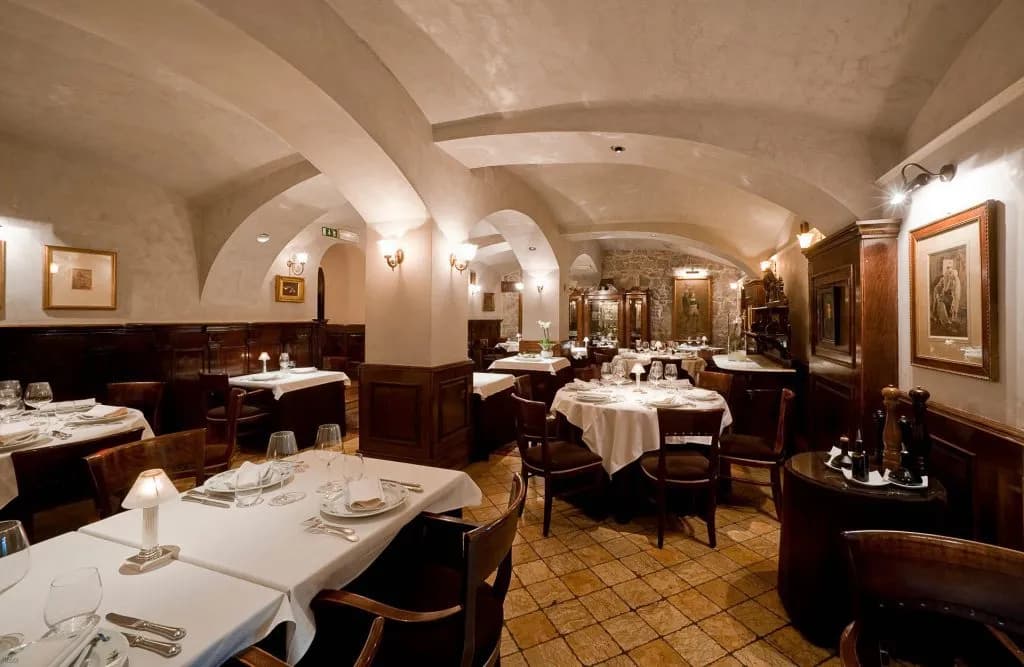 Elegant restaurant interior with vaulted ceilings, white tablecloths, and dark wood paneling in Ljubljana.