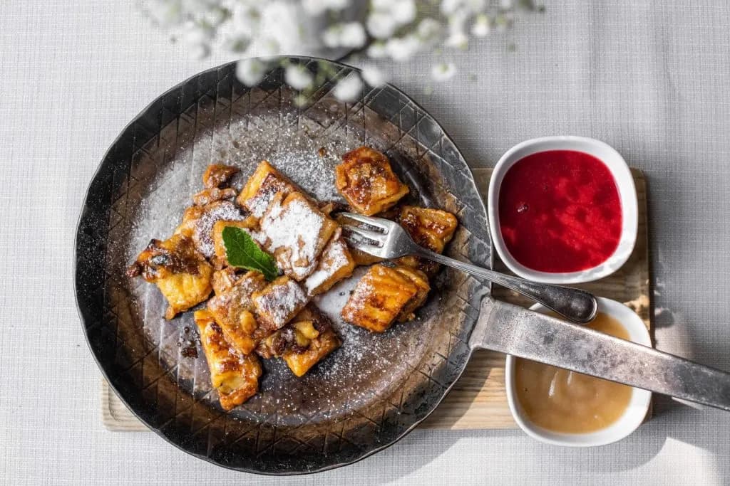 Kaiserschmarrn dusted with powdered sugar served with raspberry sauce and applesauce in a metal pan.