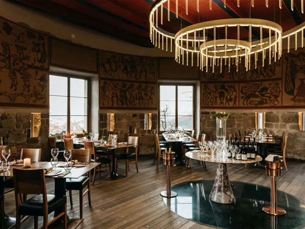 Restaurant interior in Ljubljana with stone walls, tapestries, and modern circular chandeliers.