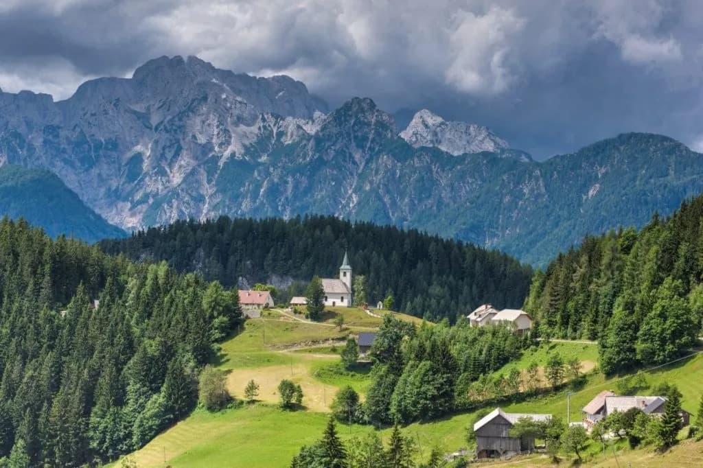 Panoramic view of a small village with a white church above Logar Valley and rugged mountains.