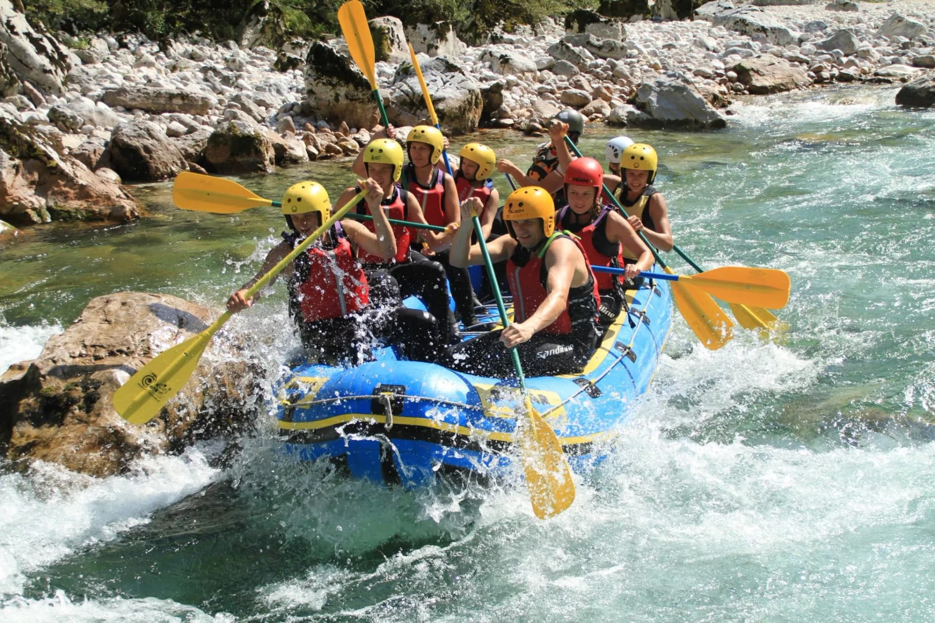 White water rafting group paddling inflatable boat through rapids near rocky river banks, Soca River.