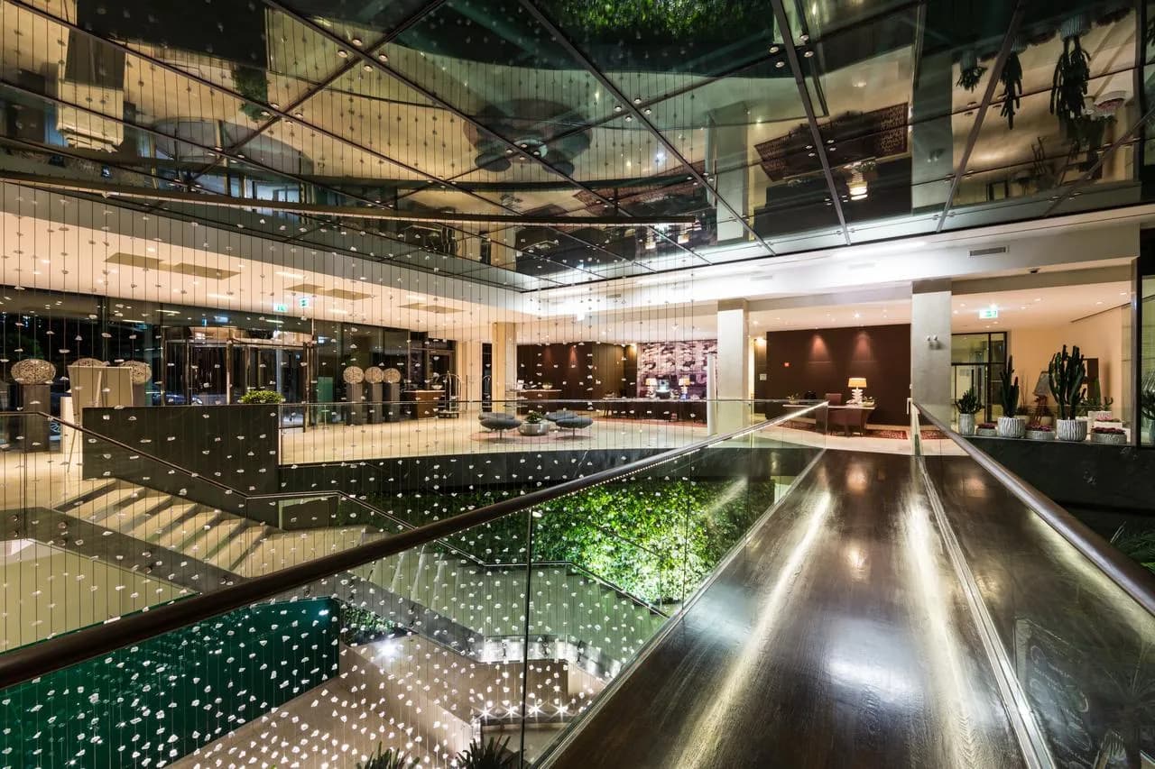 Modern hotel lobby interior with glass ceiling, wood floors, and cascading crystal light fixtures.
