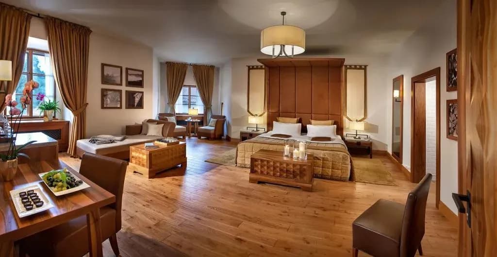 Hotel suite with wood floors, large bed, seating area, and fruit platter at Hotel Grad Otočec.
