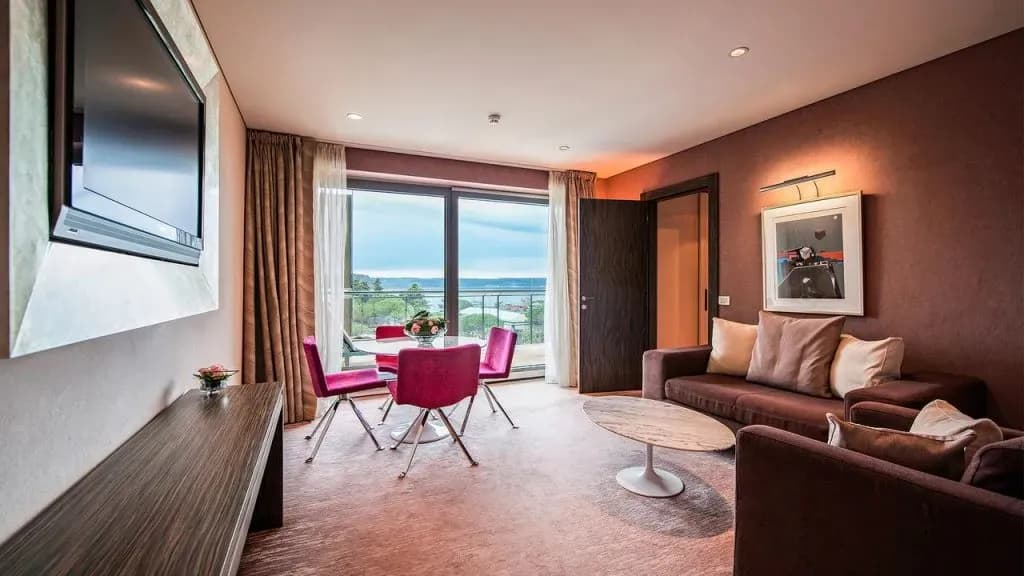 Kempinski Palace hotel room with seating area, dining table, and balcony view of the sea.