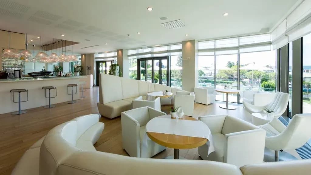 Modern hotel bar lounge with white seating, wood floors, and view of outdoor area at Kempinski Palace.