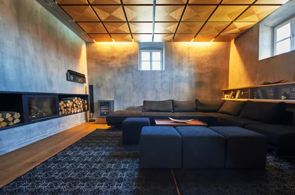 Modern lounge with dark sectional sofa, wood ceiling, and built-in fireplace with logs.