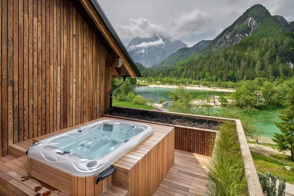 Jacuzzi on wooden balcony overlooking turquoise lake and forested mountains at Boutique Hotel Milka
