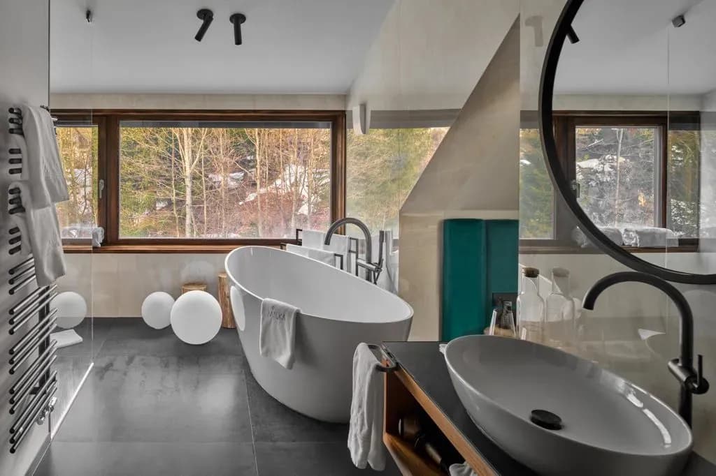 Modern bathroom with freestanding tub and sink overlooking a winter forest view.