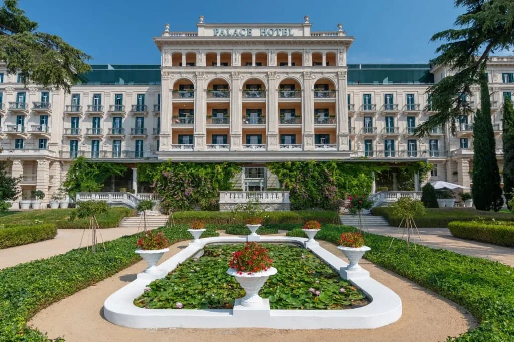 Palace Hotel Portoroz facade with formal garden and lily pond under blue sky.
