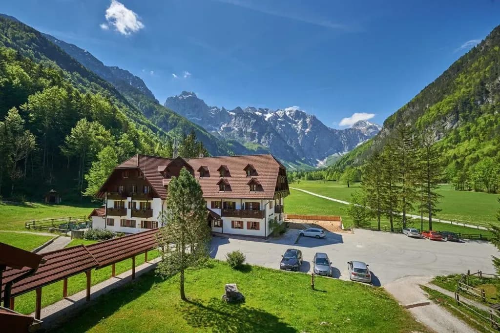 Hotel Plesnik aerial view in a green valley with snow-capped Julian Alps mountains