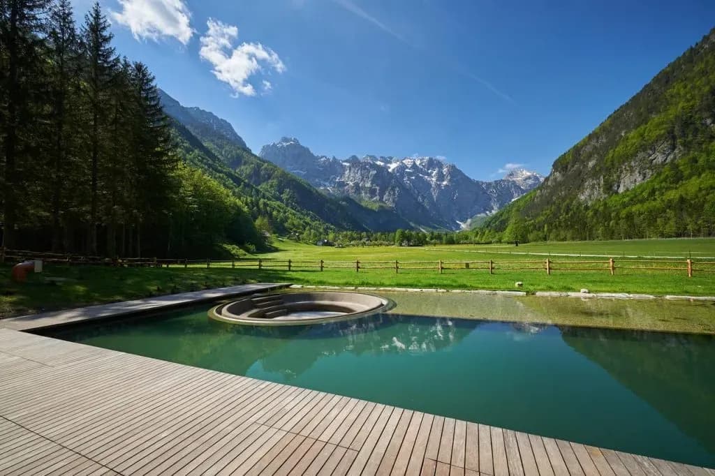 Outdoor pool with wooden deck overlooking green valley and snow-capped mountains, Hotel Plesnik.