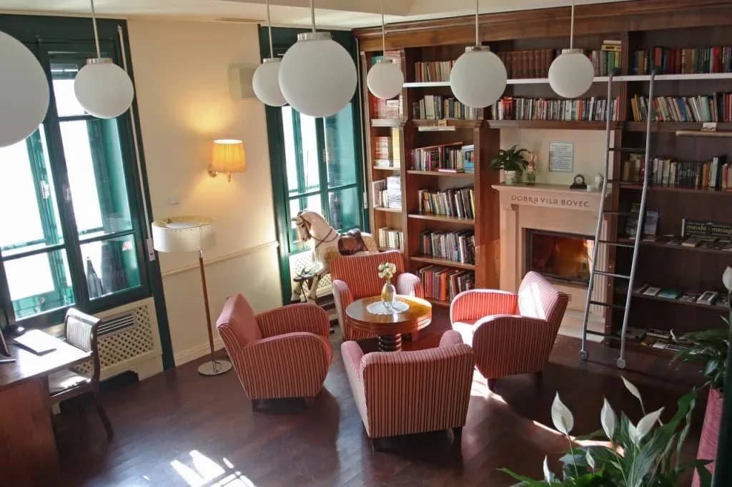 Lounge area with striped armchairs, fireplace, and floor-to-ceiling bookshelves at Dobra Vila Bovec.
