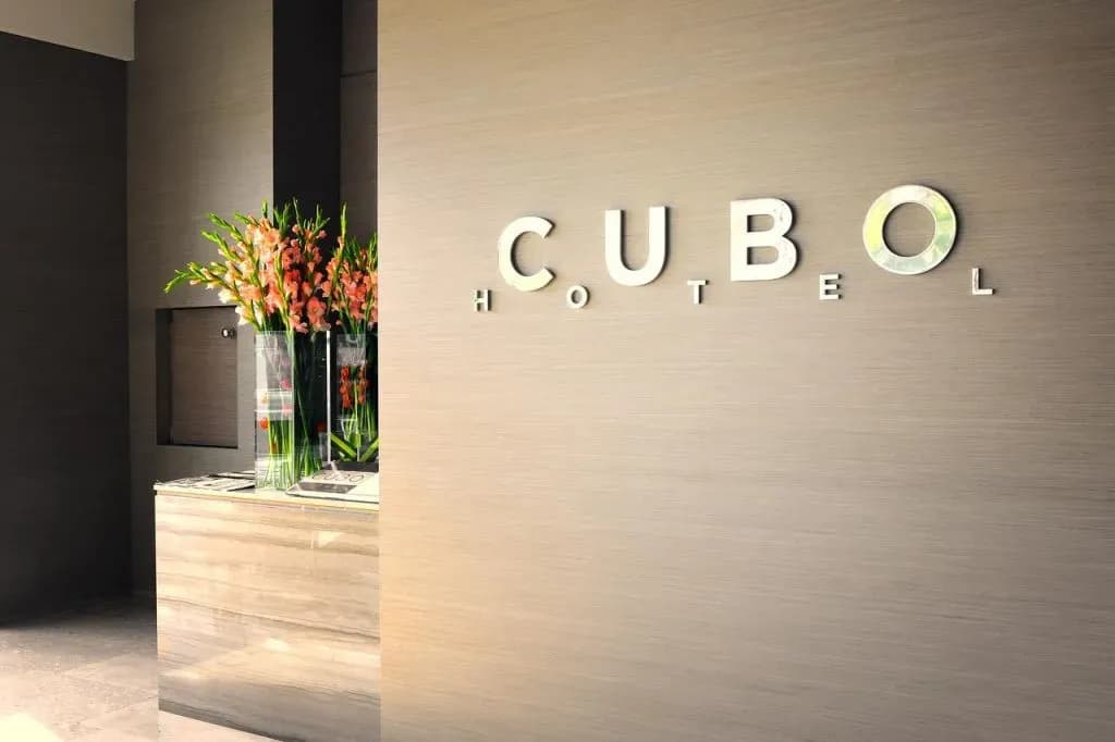 Cubo Hotel logo signage on a textured wall next to a reception desk with flowers.