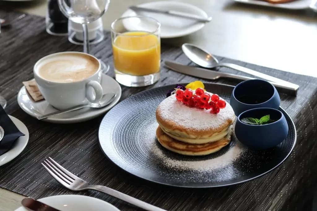 Pancakes with red currants and powdered sugar served with coffee and orange juice at breakfast.