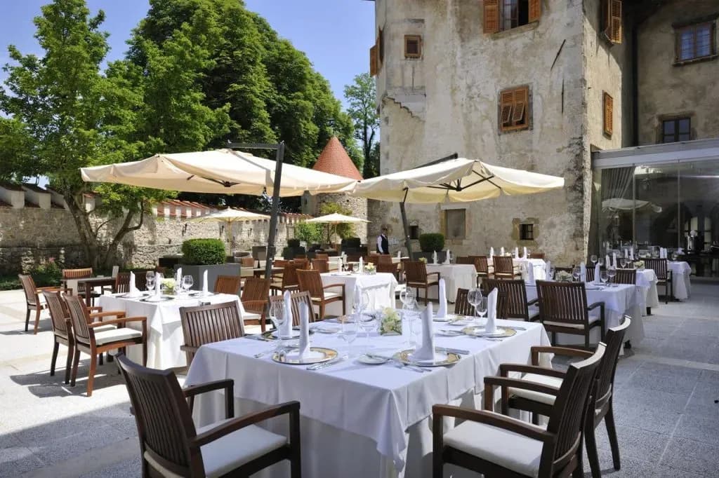 Outdoor dining courtyard with white linen tables next to a historic stone building at Hotel Grad Otočec.