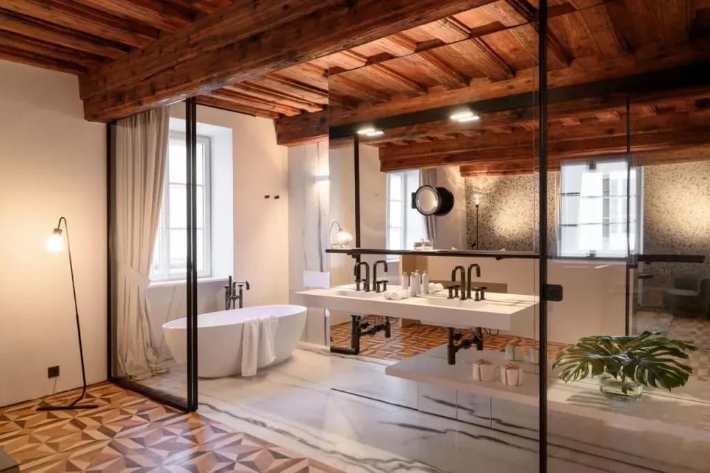 Luxury bathroom suite with freestanding tub, double vanity, wood beams, and patterned floor