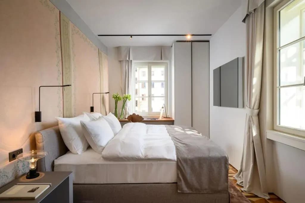 Modern hotel room with white bedding, pink patterned wall, and window view in Zlata Ladjica.
