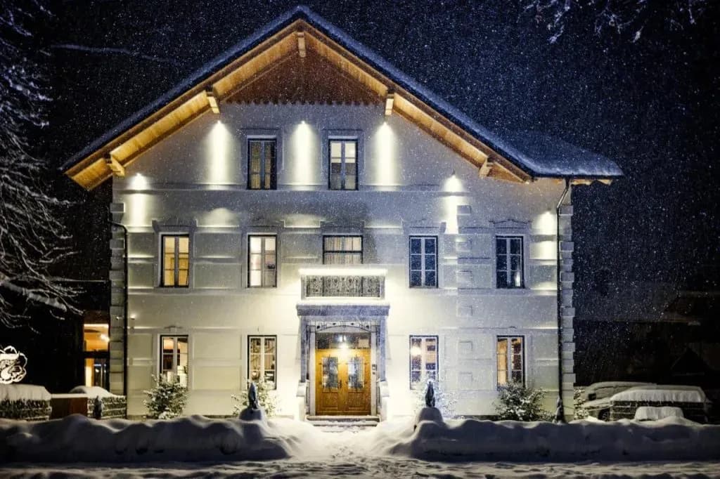 Illuminated white building at night during heavy snowfall with snow-covered ground