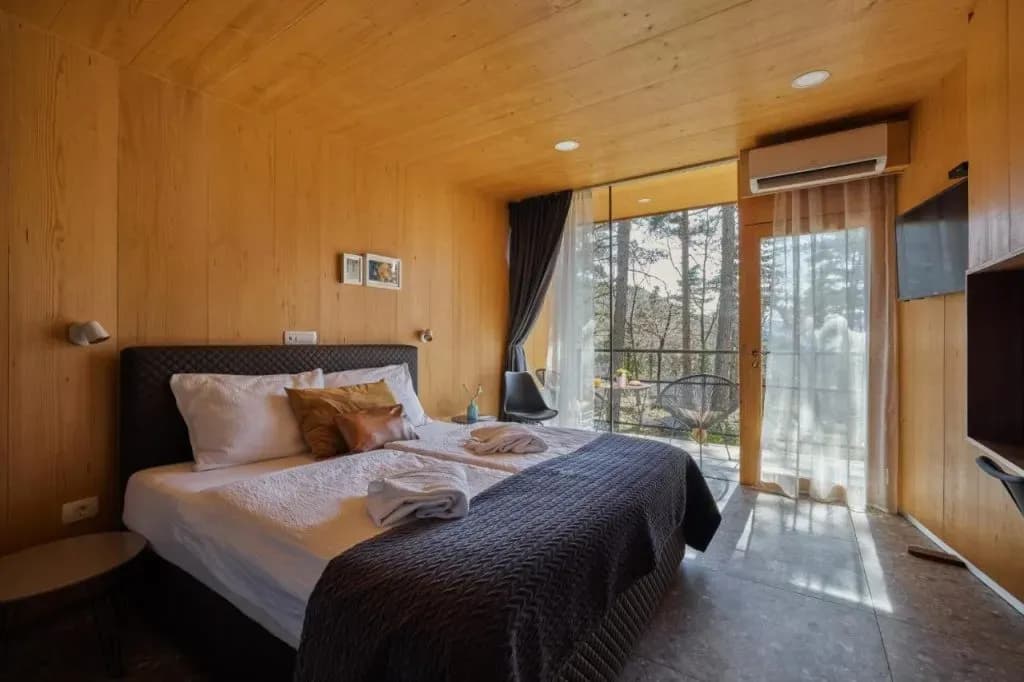 Glamping room with wood paneling, large bed, and balcony view of forest in Vipava.