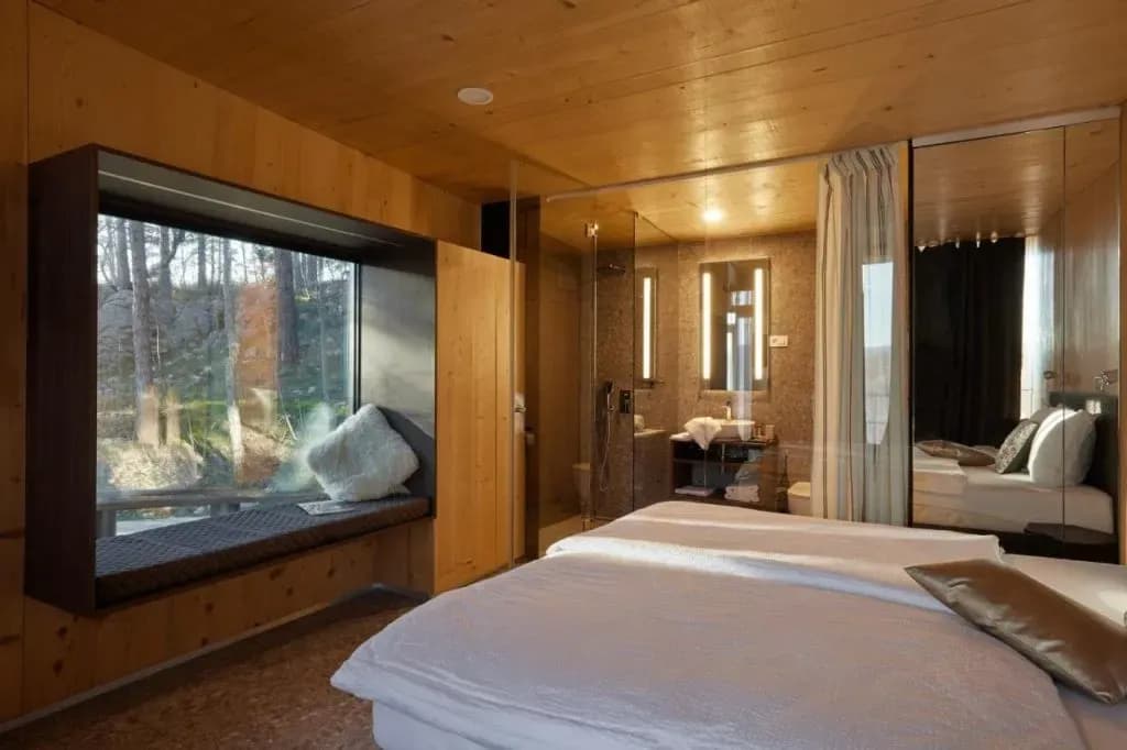 Glamping room with wood paneling, window seat overlooking forest, and open bathroom area in Vipava.