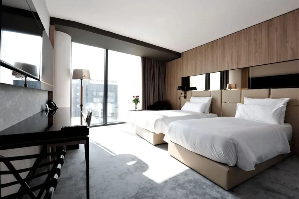 Twin beds with white linens in a modern hotel room with city view windows